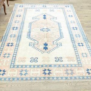 May include: A vintage cream-coloured rug with a blue and pink geometric pattern. The rug has a central medallion with a starburst design and a border with repeating stars and geometric shapes.