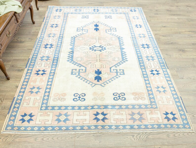 May include: A vintage cream-coloured rug with a blue and pink geometric pattern. The rug has a central medallion with a starburst design and a border with repeating stars and geometric shapes.