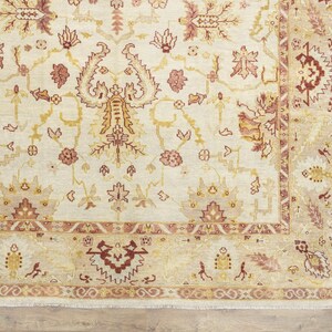 May include: A cream-colored rug with a detailed floral pattern in shades of red, brown, and gold. The rug has a border with a repeating pattern of stylized leaves and flowers.