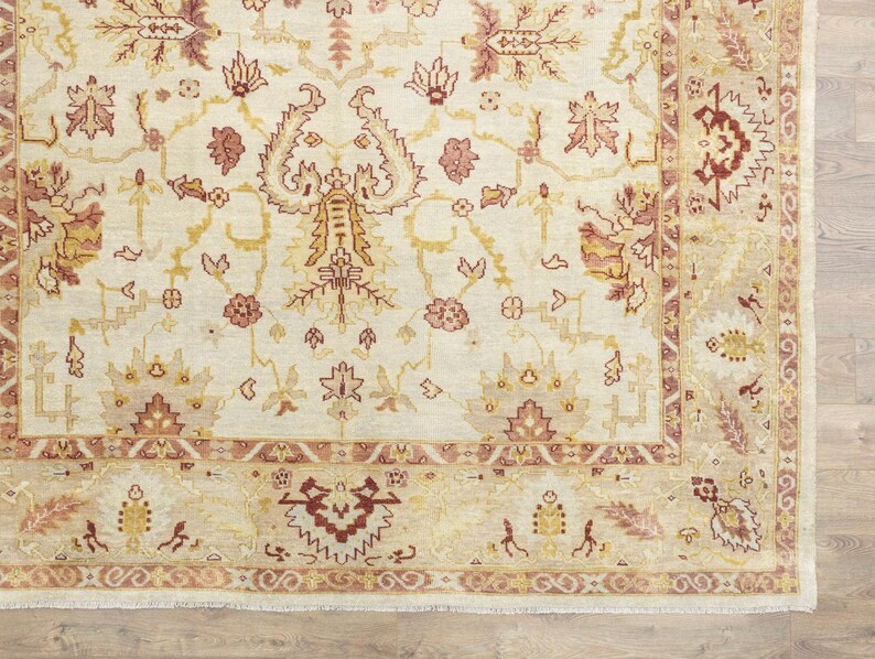 May include: A cream-colored rug with a detailed floral pattern in shades of red, brown, and gold. The rug has a border with a repeating pattern of stylized leaves and flowers.
