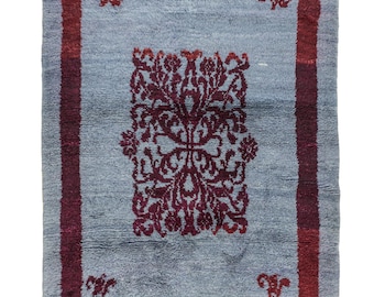 Peut inclure: Tapis rectangulaire avec un champ bleu clair et une bordure rouge foncé. Le tapis présente un motif floral central rouge foncé et de petits motifs floraux dans chaque coin. Le tapis a une frange sur le bord inférieur.