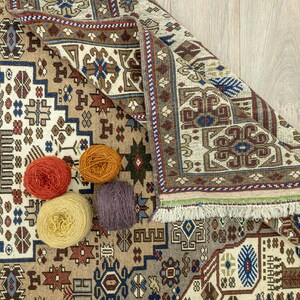 May include: A close-up of a patterned rug with a fringe border. Four balls of yarn in different colors are placed on the rug. The yarn is likely for crocheting or knitting.