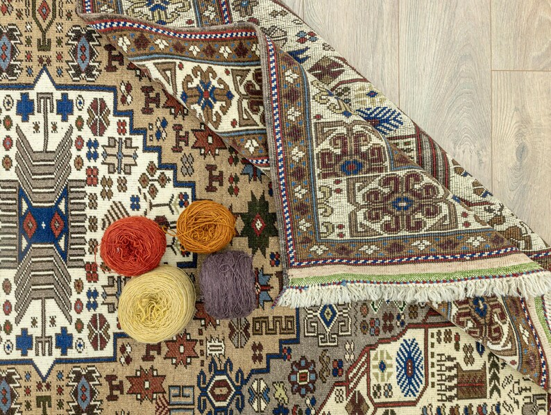 May include: A close-up of a patterned rug with a fringe border. Four balls of yarn in different colors are placed on the rug. The yarn is likely for crocheting or knitting.