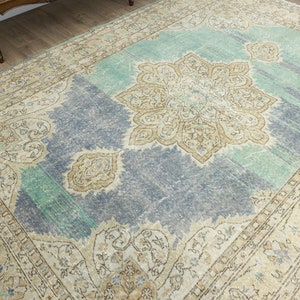 May include: A large, rectangular area rug with a distressed, vintage appearance. The rug features a central medallion design in beige and brown, surrounded by a blue and teal field. The border is a lighter beige with floral patterns.