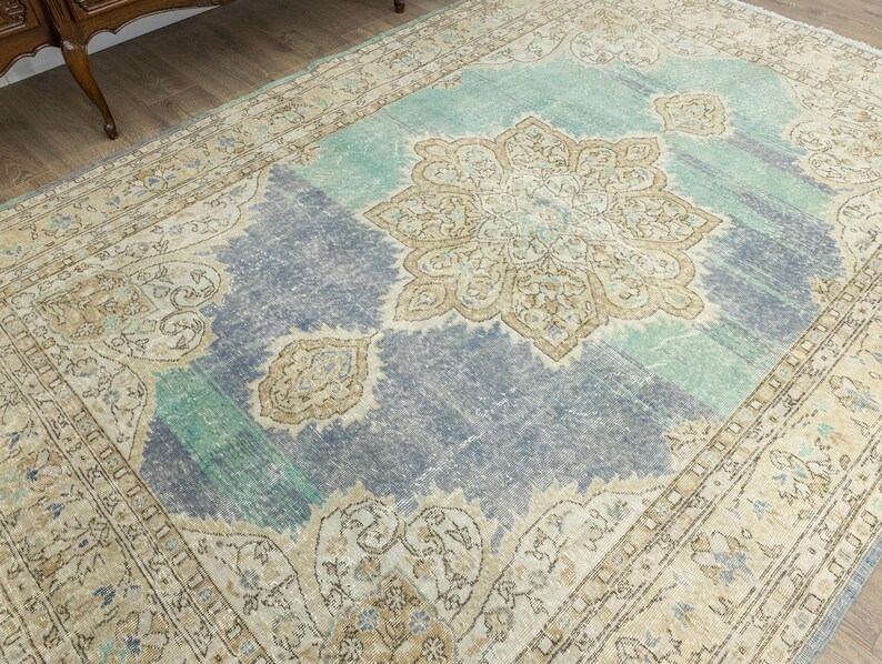 May include: A large, rectangular area rug with a distressed, vintage appearance. The rug features a central medallion design in beige and brown, surrounded by a blue and teal field. The border is a lighter beige with floral patterns.
