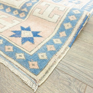 May include: A close-up of a blue and pink patterned rug with a fringed border. The rug is folded in half and the pattern is visible on both sides.