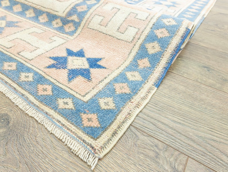 May include: A close-up of a blue and pink patterned rug with a fringed border. The rug is folded in half and the pattern is visible on both sides.