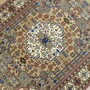 May include: A beige rug with a detailed geometric pattern in shades of brown, blue, and red. The pattern features intricate floral motifs and repeating shapes.