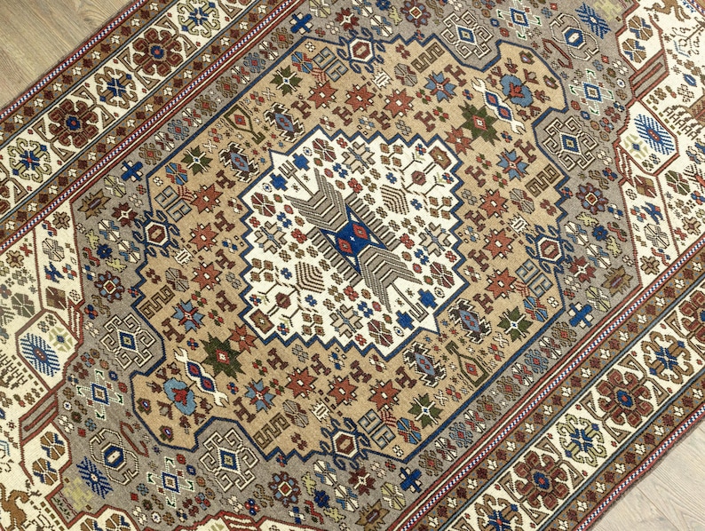 May include: A beige rug with a detailed geometric pattern in shades of brown, blue, and red. The pattern features intricate floral motifs and repeating shapes.
