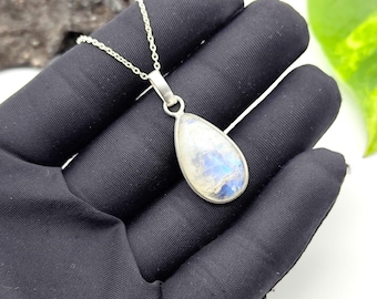 May include: A silver necklace featuring a teardrop-shaped pendant. The pendant has a pearlescent, iridescent stone with blue and white hues, set in a silver bezel. The chain is a delicate silver link.