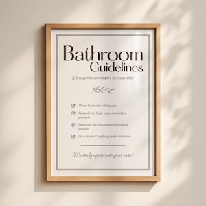 Puede incluir: Un cartel enmarcado con el texto "Bathroom Guidelines" en una fuente decorativa. El cartel incluye recordatorios sobre papel higiénico, productos sanitarios, desmaquillado y un mensaje de agradecimiento. El marco es de color marrón claro.