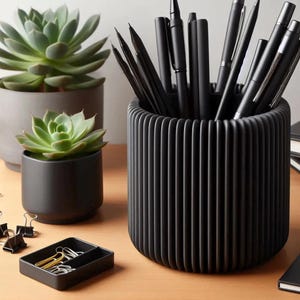May include: A black ribbed pen holder filled with black pens and pencils. Two potted succulents and a small black tray with paper clips and binder clips are also visible on a wooden surface.