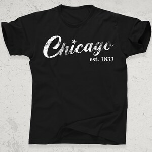 May include: Black t-shirt with the word "Chicago" in distressed white lettering, a star, and the text "est. 1833". The shirt has short sleeves and a crew neck.