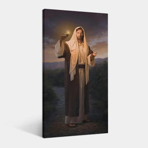 Op de afbeelding: Een canvas print met een figuur in een witte jurk en bruine mantel, met een brandende olielamp. De figuur staat op een pad met een bergachtige achtergrond en een bewolkte lucht. Het kunstwerk heeft een religieus thema.