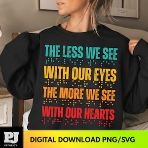 May include: Black sweatshirt with the text "THE LESS WE SEE WITH OUR EYES THE MORE WE SEE WITH OUR HEARTS" in teal, yellow, orange, and red. The text includes braille dots. The bottom of the image has the text "DIGITAL DOWNLOAD PNG/SVG".