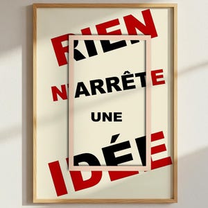 Peut inclure: Impression d'art encadrée avec le texte français « RIEN N'ARRÊTE UNE IDÉE » en noir et rouge. L'œuvre est dans un cadre en bois clair, avec un cadre plus petit et vide qui chevauche le texte. Le fond est de couleur crème.