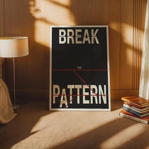 Peut inclure: Une affiche encadrée en noir et blanc avec les mots "BREAK THE PATTERN" en lettres blanches en gras. Une ligne rouge relie les mots. Une pile de livres est posée sur le sol à côté de l'affiche. Une lampe et un lit beiges sont en arrière-plan.