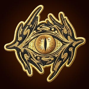 Könnte beinhalten: Ein gestickter Aufnäher mit einem zentralen Auge, das eine vertikale schwarze Pupille und eine goldene Iris aufweist. Das Auge ist von komplexen, geschwungenen schwarzen und goldenen Fadenmustern umgeben, die eine scharfe, organische Form bilden.