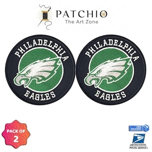 May include: Two circular patches featuring the Philadelphia Eagles logo. The patches have a black border, a green center with a white eagle head, and the words "PHILADELPHIA EAGLES" in white. The image also includes the text "PATCHIO The Art Zone".