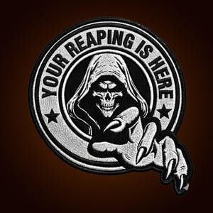 Könnte beinhalten: Ein kreisförmiger bestickter Aufnäher mit einem schwarz-weißen Design einer Kapuzen-Totenkopffigur mit einem dritten Auge. Der Text "YOUR REAPING IS HERE" ist entlang des oberen Randes gebogen und von zwei Sternen flankiert. Eine Skeletthand ragt aus der Mitte hervor.