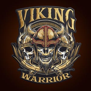 May include: An embroidered patch featuring the text VIKING WARRIOR in gold thread. The design displays a central skull wearing a horned helmet flanked by two additional skulls in horned helmets, all accented with gold and black stitching.