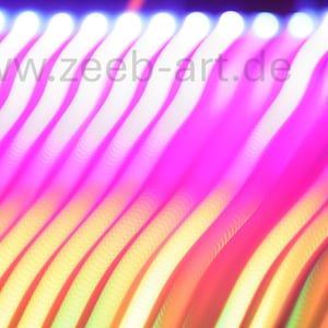 May include: A long exposure light trail photograph featuring diagonal, wavy lines of vibrant magenta, yellow, and orange hues against a dark background. The text www.zeeb-art.de is visible in the upper portion of the image, overlaid on the light.