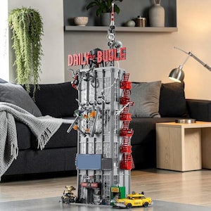 Peut inclure: Un modèle LEGO détaillé du bâtiment Daily Bugle, avec une enseigne rouge, des échelles de secours et un taxi jaune. Le bâtiment est gris avec de nombreuses fenêtres et des figurines attachées. Le modèle est posé sur un sol en bois.