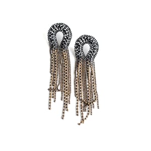 May include: A pair of dangling earrings. Each earring features a loop-shaped top encrusted with black and silver beads. Below the loop, strands of small, bronze-colored beads cascade downwards, creating a fringe effect. The earrings are set against a white background.