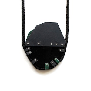 Puede incluir: Un collar de cuero negro con un colgante geométrico. El colgante está hecho de cuero negro y verde y tiene un cordón parecido a una cuerda.