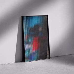 May include: Abstract art print in a black frame. The artwork features a blurred, vertical striped design with colors of blue, red, and black. The framed art is leaning against a white wall on a gray concrete floor.