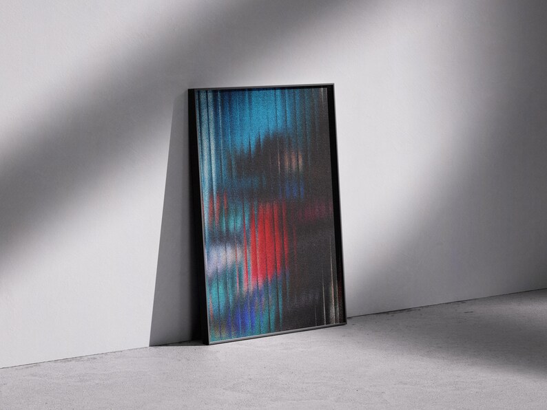 May include: Abstract art print in a black frame. The artwork features a blurred, vertical striped design with colors of blue, red, and black. The framed art is leaning against a white wall on a gray concrete floor.