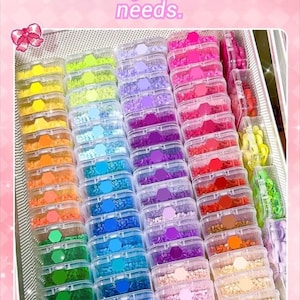 May include: Rows of small, clear plastic containers filled with colourful beads and sequins. The containers are arranged to display a vibrant colour palette. Text at the top reads "Vibrant Color Palette - Meets all your creative needs."