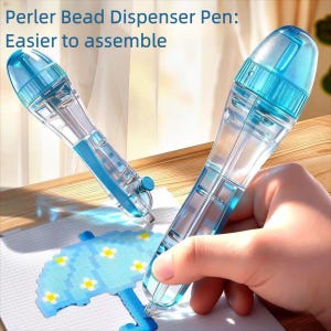 Puede incluir: Dos bolígrafos dispensadores de cuentas Perler transparentes con detalles azules. Los bolígrafos están etiquetados como "Perler Bead Dispenser Pen: Easier to assemble." Una mano sostiene un bolígrafo, dispensando cuentas sobre un diseño de paraguas azul. Los bolígrafos están diseñados para un fácil montaje de cuentas.