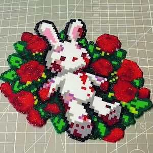 May include: A pixel art design of a white rabbit with pink ears and red details, set amongst red roses and green foliage. The image is created using small, colourful beads, giving a textured appearance.