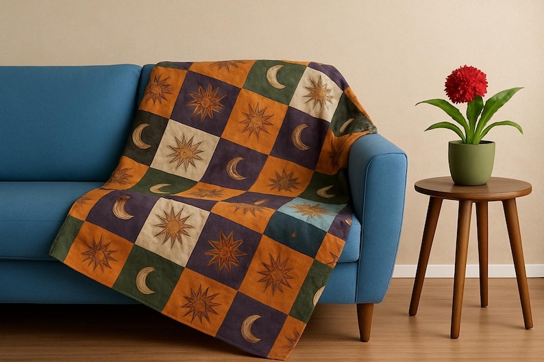 May include: A patterned throw blanket with sun and moon motifs in a checkerboard design, draped over a blue sofa. A red flower in a green pot sits on a wooden side table. The blanket's colors include orange, green, and purple.
