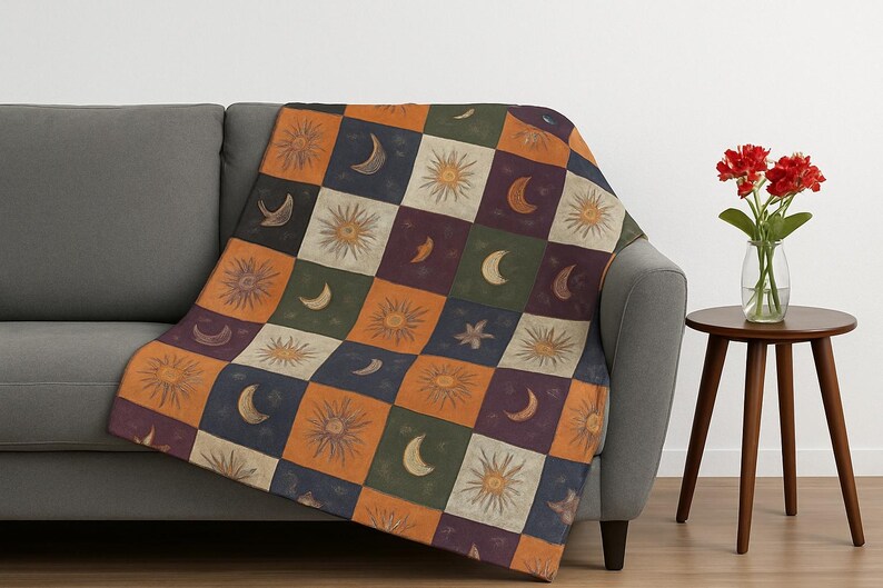 May include: A patterned throw blanket featuring suns, moons, and stars in a patchwork design. The blanket is draped over a grey sofa. The colour scheme includes orange, green, purple, and cream.