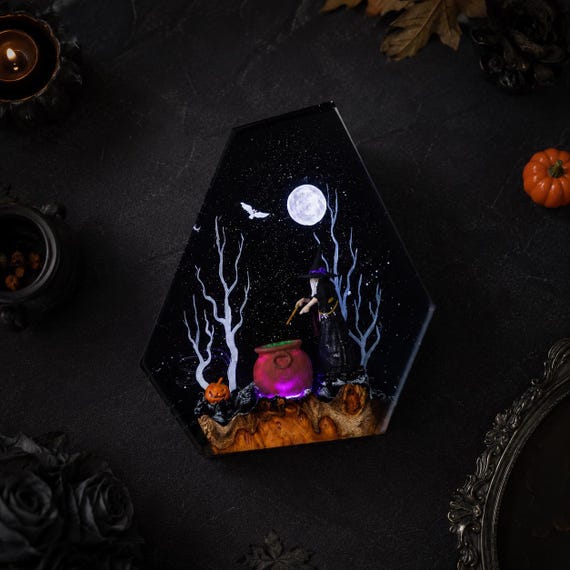 A hand-poured resin diorama lamp with a glowing witch cauldron, moonlit sky, and real wood elements — tiny spooky world you can actually light up.