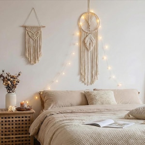 May include: A bedroom scene featuring macrame wall hangings, a bed with neutral-toned bedding, and a wooden nightstand. A lit dreamcatcher hangs above the bed, with string lights adding a warm glow. A vase of dried flowers sits on the nightstand.