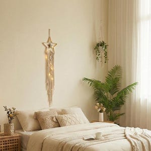 Puede incluir: Una escena de dormitorio con una paleta de colores neutros. Una cama está hecha con ropa de cama beige, almohadas decorativas y una manta con flecos. Un adorno de pared en forma de estrella con luces está sobre la cama. Una planta colgante y una planta en maceta añaden vegetación.