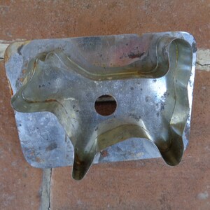 May include: A vintage metal cookie cutter in the shape of a cow. The cutter is made of silver-colored metal with a slightly rusted appearance. It features a circular hole and is designed for cutting dough into cow shapes.