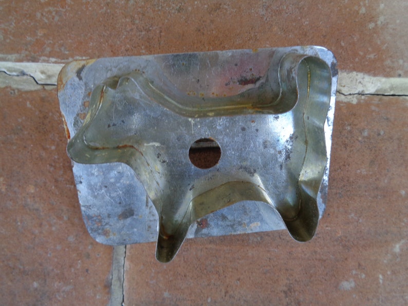 May include: A vintage metal cookie cutter in the shape of a cow. The cutter is made of silver-colored metal with a slightly rusted appearance. It features a circular hole and is designed for cutting dough into cow shapes.