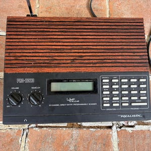 Puede incluir: Un escáner programable de 20 canales Realistic PRO-2023 con panel superior de imitación madera, frontal negro con dos perillas de volumen y squelch, pantalla digital y teclado numérico con varios botones de función integrados.