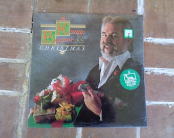 May include: Album cover for Kenny Rogers' Christmas album. The cover features a portrait of Kenny Rogers, with the title "Christmas" below his name. He is holding a gift box with a red bow.