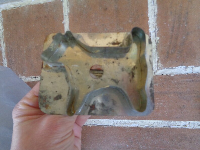 May include: Vintage metal dog-shaped cookie cutter. The cutter has a rectangular base with a dog silhouette cut out. The metal has a worn, aged appearance with some rust spots, suggesting it's an antique kitchen tool.