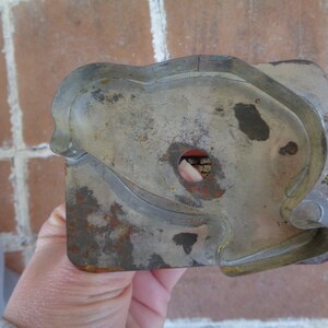 May include: A vintage, rectangular cookie cutter with a heart-shaped design. The metal cutter has a worn, aged appearance with areas of rust and discoloration. The cutter has a small hole in the center.