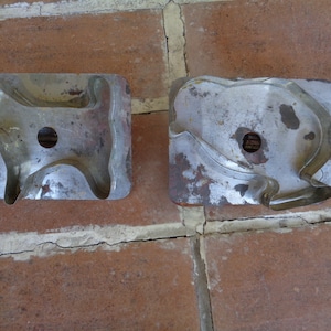 May include: Two vintage metal cookie cutters. One is shaped like a dog, the other like a cat. Both are rectangular with a cutout design and a central hole. The metal has a worn, aged appearance.