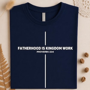 Peut inclure: T-shirt bleu marine avec l'inscription blanche "FATHERHOOD IS KINGDOM WORK" et "PROVERBS 22:6". Un motif de croix blanche est centr&eacute; sur le t-shirt. Le t-shirt est en tissu doux.