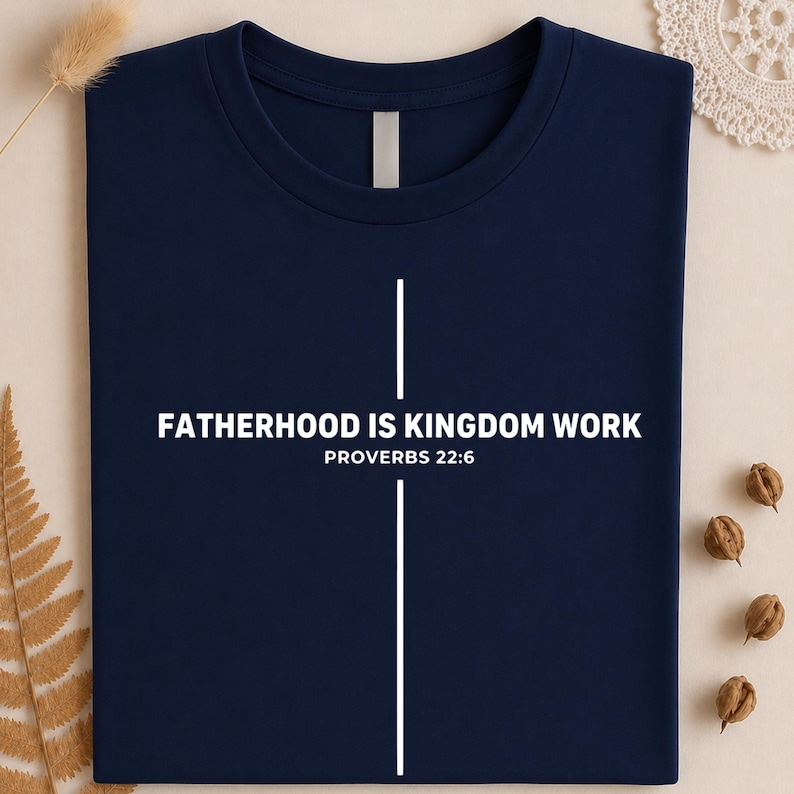 Peut inclure: T-shirt bleu marine avec l'inscription blanche "FATHERHOOD IS KINGDOM WORK" et "PROVERBS 22:6". Un motif de croix blanche est centr&eacute; sur le t-shirt. Le t-shirt est en tissu doux.