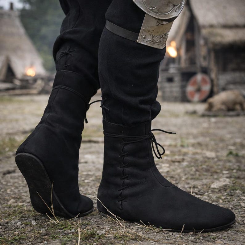 May include: Black suede-like boots with a pointed toe and lace-up detailing. The boots are mid-calf height and appear to be worn in an outdoor setting. The boots are part of a historical or fantasy costume.