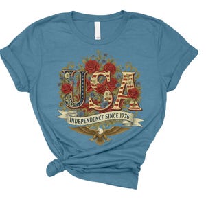 May include: A light blue t-shirt with the word "USA" in a floral design, incorporating red roses and the American flag pattern. The text "INDEPENDENCE SINCE 1776" is on a banner below "USA", with an eagle graphic at the bottom.